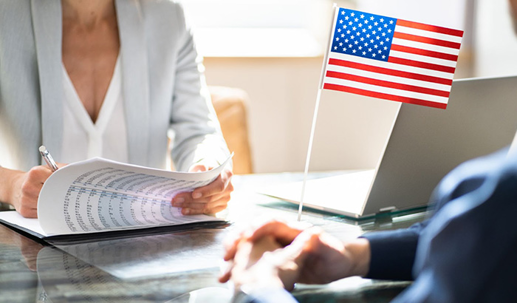 A man and a woman sit in a table with a laptop and flag.